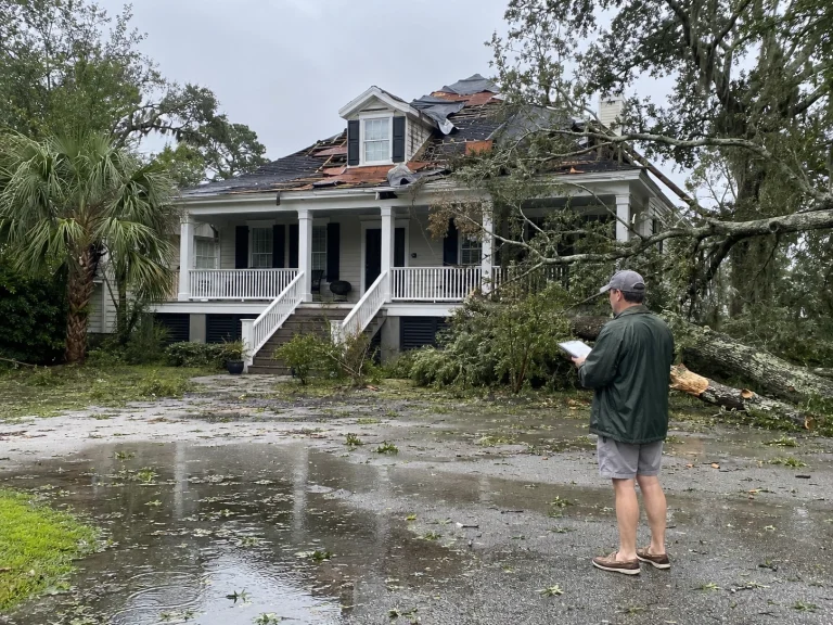 Homeowner documenting storm damage at a Lowcountry home with roof damage, flooding, debris, and a fallen tree limb.